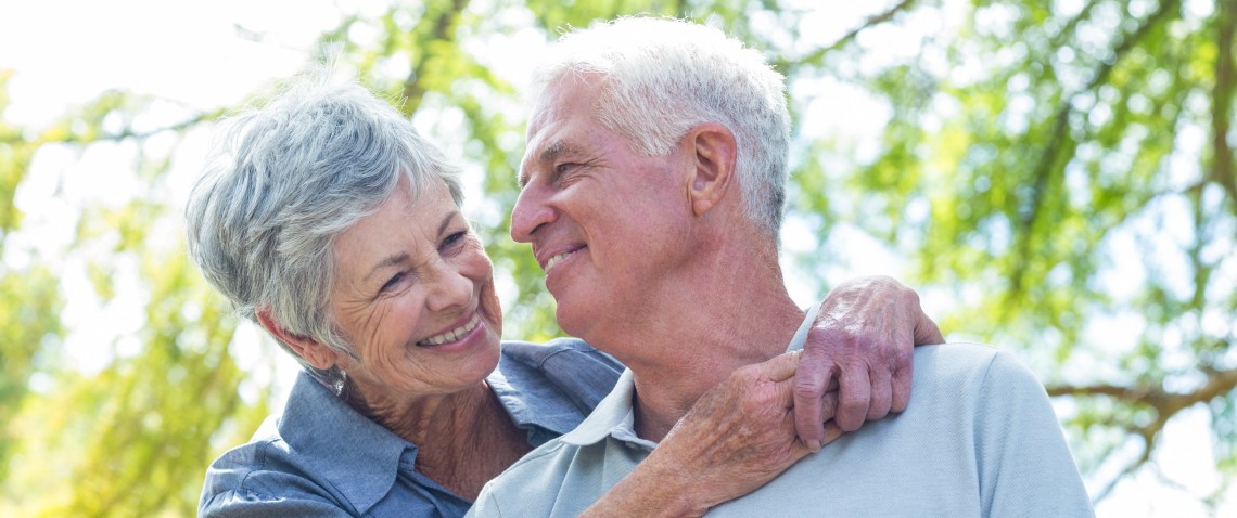 Elderly couple with grey hair, look supportive and lovingly at each other, embracing near a tree.