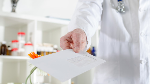 Doctor in white coat with arm stretched out handing patient a referral for therapy in white envelope.