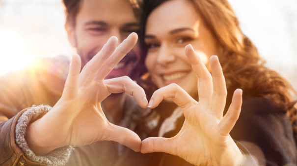 Young couple, look happy and harmonious as they create a heart shape with their fingers and thumbs.