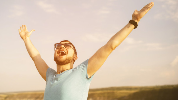 Young man with glasses, throwing arms up into the air and looking up to the sky with confidence.