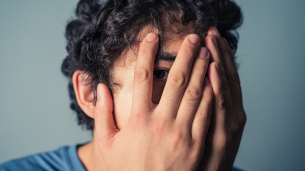 Young man looking frightened with his hands covering his face.