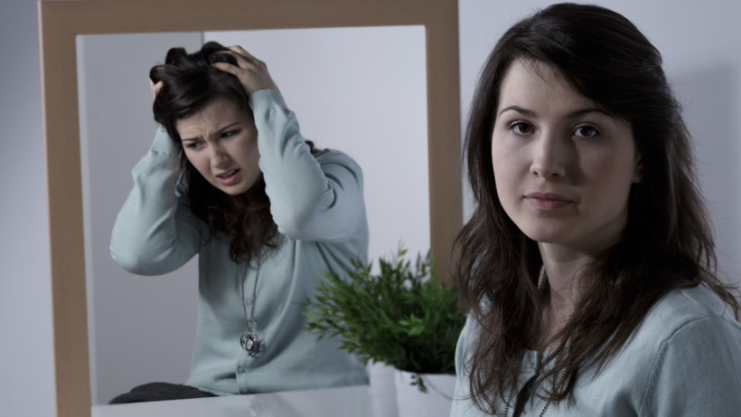 Calm relaxed looking woman, see's herself in the mirror as being very stressed, confused and upset.