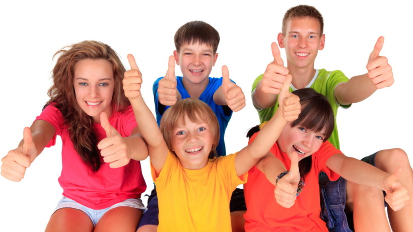 Two adolescent teenagers and three younger children in bright plain tee-shirts, showing thumbs up and big smiles.